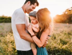 Parents embracing their young child in a sunlit field, symbolizing warmth, connection, and the joy of family bonds.
